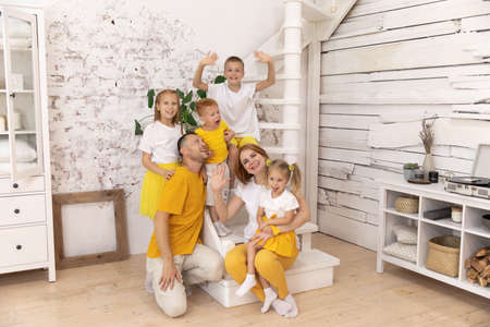 the whole family is wearing white and yellow T-shirts. a happy family at home sits on the stairs. parents and children have a great time togetherの写真素材