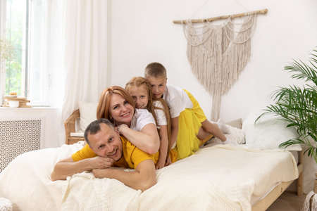 Portrait of beautiful young mother, father and their kids looking at camera and smiling while lying on bed leaning on each other. Copy spaceの写真素材