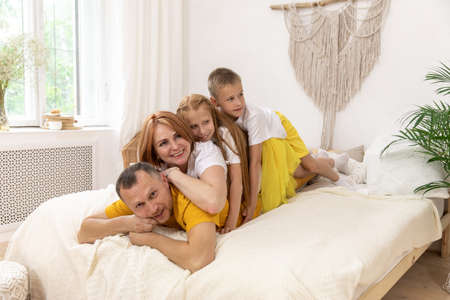Portrait young mother, father and their kids looking at camera and smiling while lying on bed leaning on each other. Copy spaceの写真素材