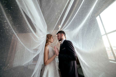 beautiful wedding couple. bride with a long white veil and in a wedding dress. groom in a stylish suit. dark interior. a lot of fataの写真素材