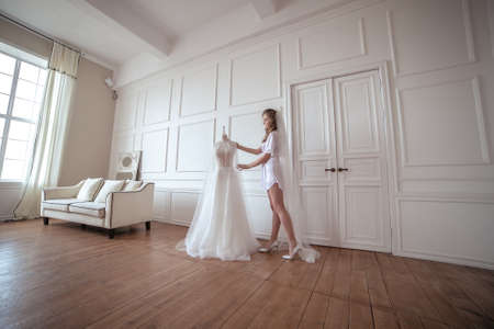 bride morning. a girl in a white robe and veil stands next to a wedding dressの写真素材