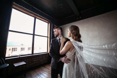beautiful wedding couple. bride with a long white veil and in a wedding dress. groom in a stylish suit. dark interiorの写真素材