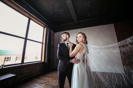 beautiful wedding couple. bride with a long white veil and in a wedding dress. groom in a stylish suit. dark interiorの写真素材