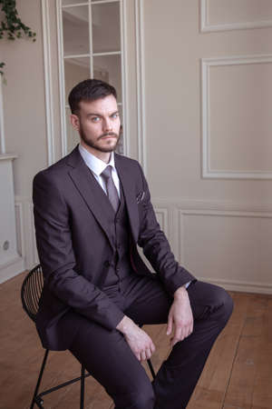 beautiful young man with a beard brunette model. guy in a classic suit in a light stylish interior. groom. portraitの写真素材