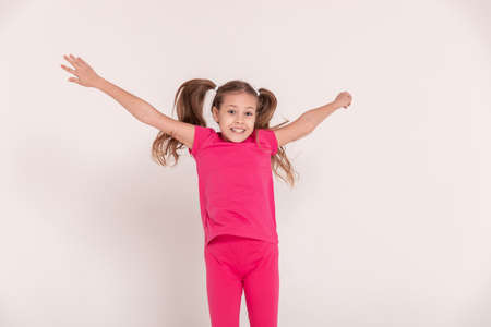a beautiful girl in a pink jumps and smiles on a white background. happy childhood. copy spaceの写真素材
