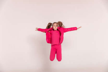 a beautiful girl in a pink jacket jumps and smiles on a white background. happy childhood. copy...