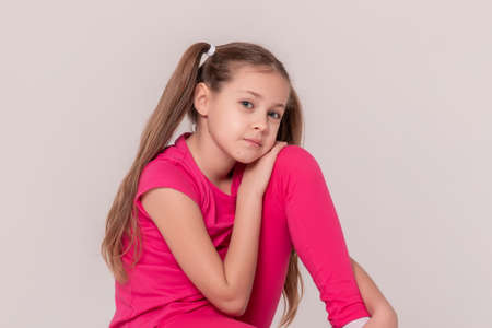 beautiful sports girl in a pink T-shirt and pants on a white isolated background. child sitting on a...
