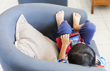 Children play with tablet PC on a blue sofaの写真素材