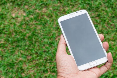 blank screen mobile phone in hand on green grass backgroundの写真素材