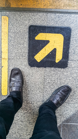 feet standing behind of the edge of a yellow line and yellow arrow on the stone floor
