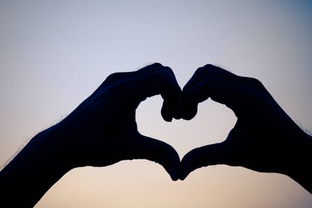 Love sign. Heart symbol by hand silhouette in sunset sky. Vintage style backgroundの写真素材