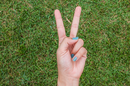 Woman hand holding up the peace sign or number two with two fingers on green grass background textureの写真素材
