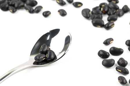 Close up of black beans on the spoon  isolated on white background