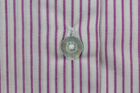 Close-up of white button on striped red and white shirt pattern