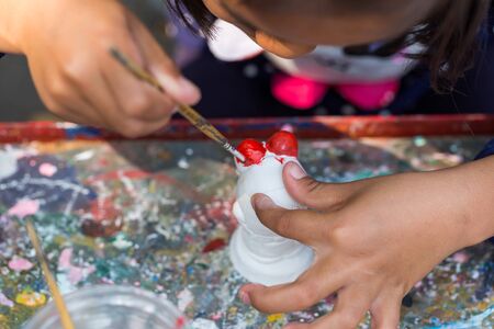 A child paints the colors of white plaster doll toys on the table