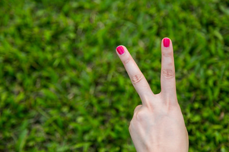 Woman hand with red nail show peace sign or number two with two fingers on green grass backgroundの写真素材