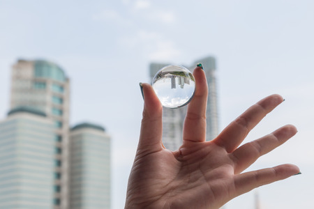 Woman hand holding a crystal ball with office building inside inverted backgroundの写真素材