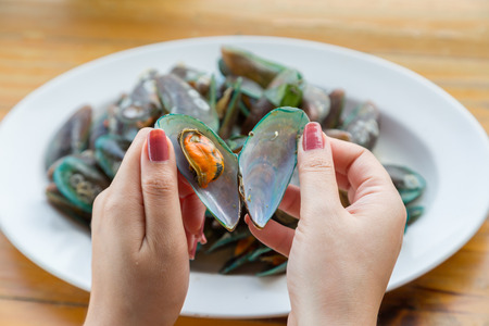 Woman hand open green mussel with white disk backgroundの写真素材