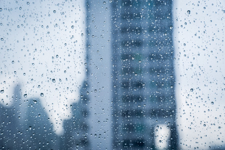 Abstract image of Rain drops on the dirty glass windows with modern office building background