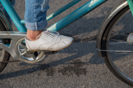 Female wearing jeans and wearing white shoes rides bicycle on the parkの写真素材
