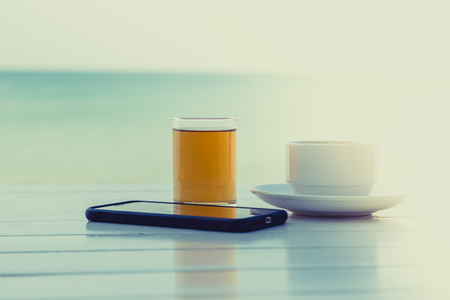 Tea coffee with smart phone on the white wooden table at the beach backgroundの写真素材