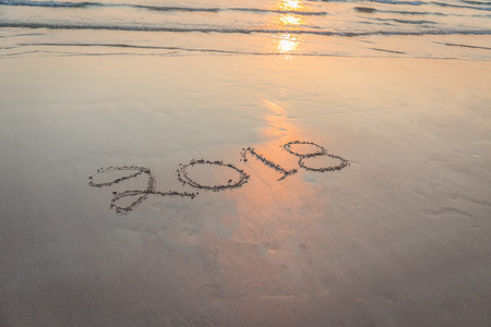 Numbers 2018 handwritten on sand at the beach during sunset time backgroundの写真素材