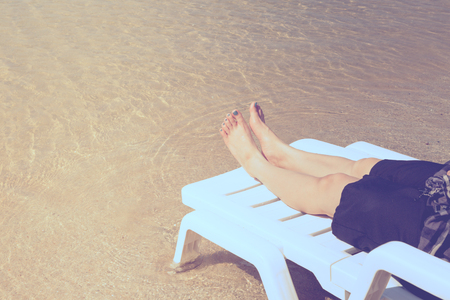 Vacation on tropical beach Woman's legs on the beach bed with clear ocean water backgroundの写真素材