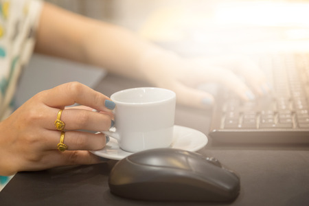 Woman hand holdding coffee cup with working table background