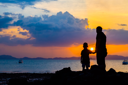 Silhouette image of father and son at the beach before sunset backgroundの写真素材