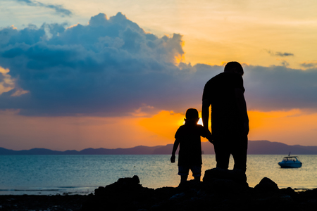 Silhouette image of father and son at the beach before sunset backgroundの写真素材