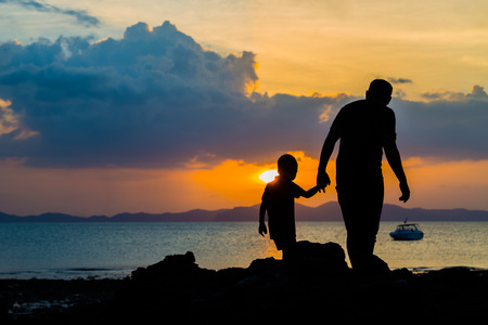 Silhouette image of father and son at the beach before sunset backgroundの写真素材