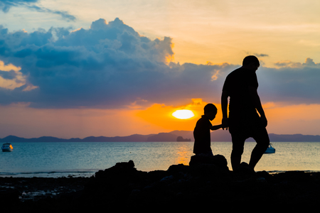 Silhouette image of father and son at the beach before sunset backgroundの写真素材