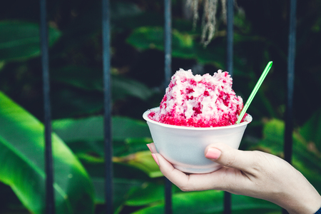 Ice desserts with topping red Syrup and sweet milk in women hand holding in nature backgroundの写真素材