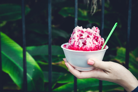 Ice desserts with topping red Syrup and sweet milk in women hand holding in nature backgroundの写真素材