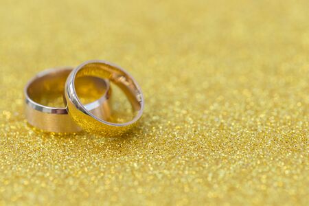 Gold wedding rings of bride and groom on gold gliter backgroundの写真素材