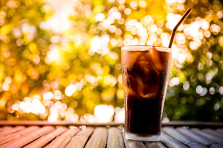 Beverage glass with ice cubes on bamboo table and bokeh backgroundの写真素材