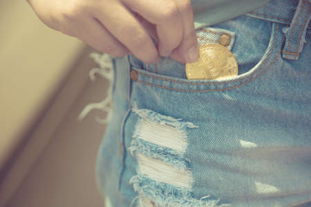 A closeup of a woman putting bitcoin cryptocurrency coin in a blue jeans pocket,Cashless Society...