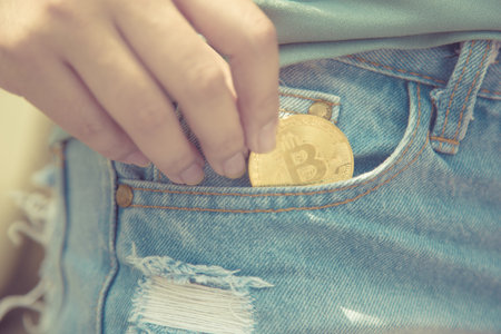 A closeup of a woman putting bitcoin cryptocurrency coin in a blue jeans pocket,Cashless Society conceptの写真素材