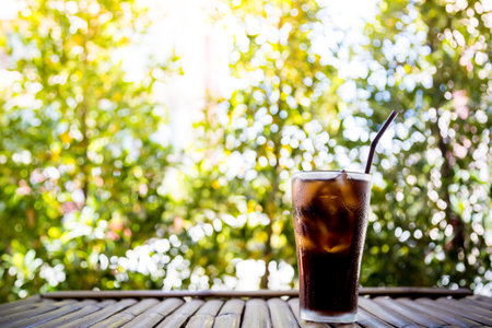 Beverage glass with ice cubes on bamboo table and bokeh backgroundの写真素材