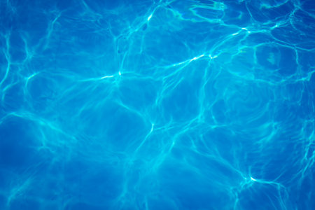 Clear blue swimming pool water with sunlight reflections creating abstract patterns and ripples.の写真素材