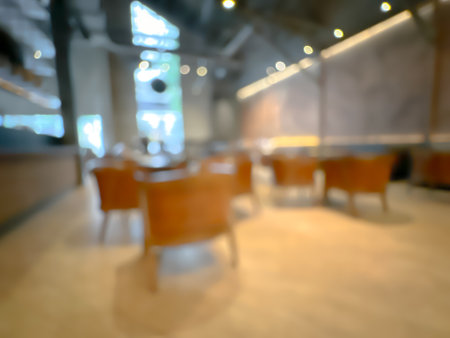 Blurred interior of a modern cafe with wooden chairs and tables, warm lighting, and large windows.の写真素材
