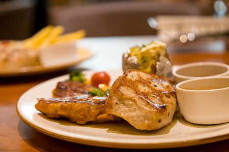 Grilled pork steak with french fries and sauce on wooden table.