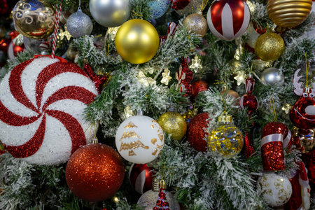 Decorated Christmas tree with vibrant ornaments, including red, gold, and silver baubles, candy canes, and festive figurines, surrounded by frosted branches and warm fairy lights creating a festive holiday ambiance.の写真素材