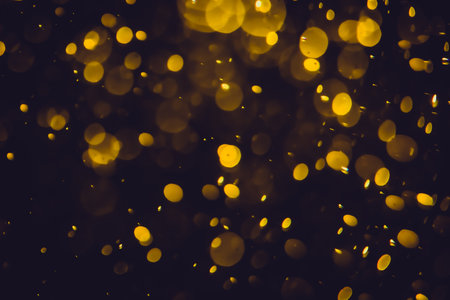 Defocused golden bokeh lights of different sizes and colors on a dark background.の写真素材