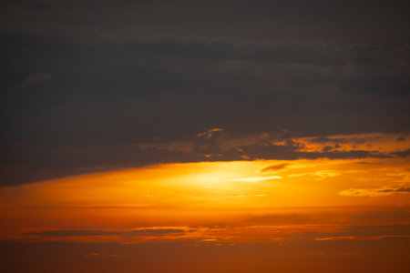 The sun dips below the horizon, casting a golden glow over the calm sea. A gentle breeze ruffles the water as a lone sailboat glides peacefully across the bay. Seagulls cry overhead, adding to the tranquil atmosphere.の写真素材