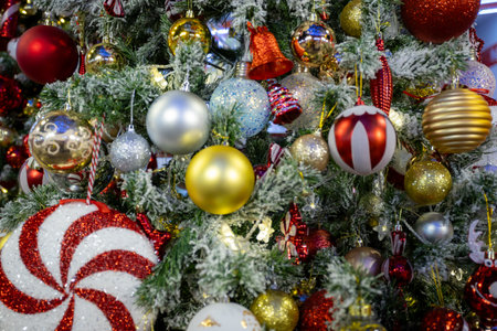 Decorated Christmas tree with vibrant ornaments, including red, gold, and silver baubles, candy canes, and festive figurines, surrounded by frosted branches and warm fairy lights creating a festive holiday ambiance.の写真素材