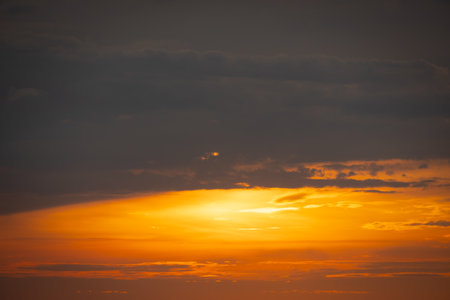 The sun dips below the horizon, casting a golden glow over the calm sea. A gentle breeze ruffles the water as a lone sailboat glides peacefully across the bay. Seagulls cry overhead, adding to the tranquil atmosphere.の写真素材