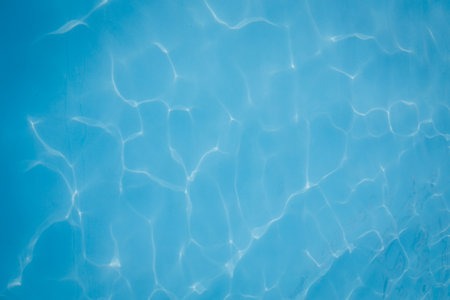 Close-up of clear blue swimming pool water with gentle sunlight reflections creating abstract patterns.の写真素材