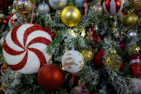 Decorated Christmas tree with vibrant ornaments, including red, gold, and silver baubles, candy canes, and festive figurines, surrounded by frosted branches and warm fairy lights creating a festive holiday ambiance.の写真素材