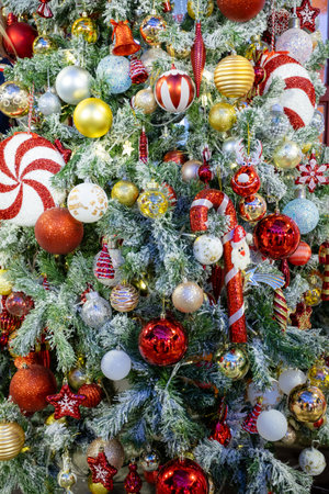 Decorated Christmas tree with vibrant ornaments, including red, gold, and silver baubles, candy canes, and festive figurines, surrounded by frosted branches and warm fairy lights creating a festive holiday ambiance.の写真素材